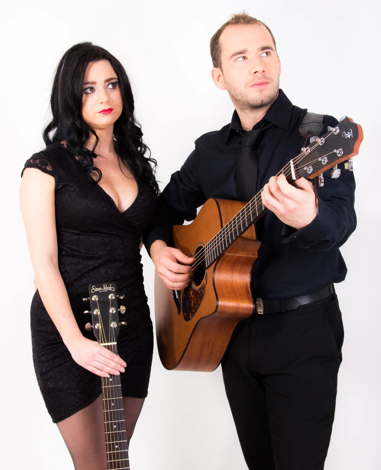 A picture of Double Malt Duo standing, each holding an acoustic guitar and looking away from camera.